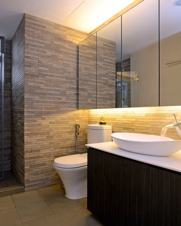 Phòng tắm ấn tượng trong mẫu thiết kế căn hộ với bức tường đá và hệ tủ gương sạch sẽ và rộng rãi.